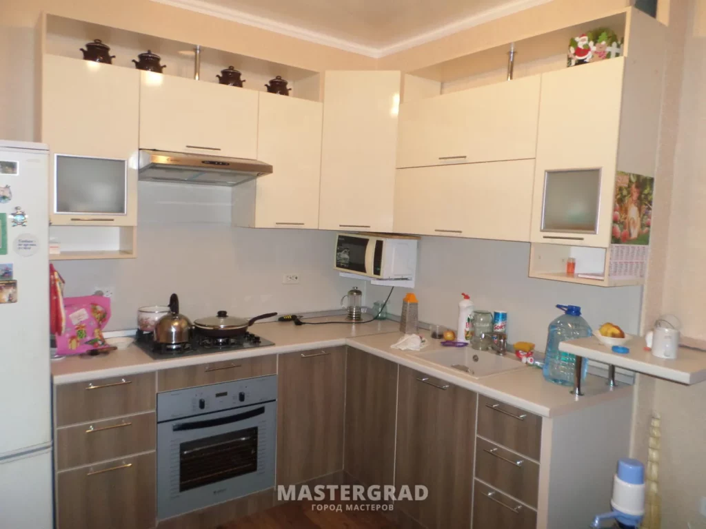 Угловая кухня с бежевыми глянцевыми фасадами и барной стойкой